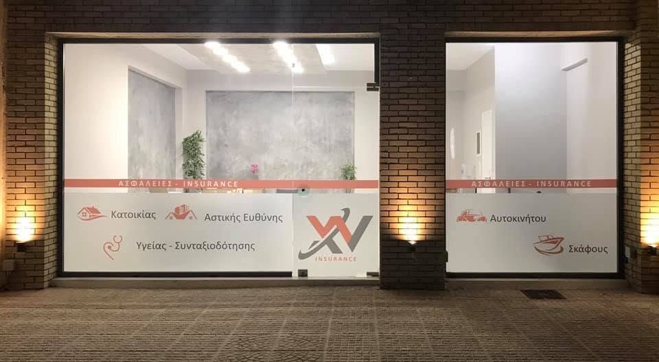 Η πρόσοψη του γραφείου XV Insurance στην Παιανία, φωτισμένη τη νύχτα. Δύο τζάμια με τις ασφαλίσεις τυπωμένες και το σήμα XV στην πόρτα.